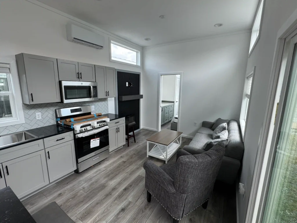 Open concept living area and kitchen inside a two bedroom park model tiny home with grey cabinetry.