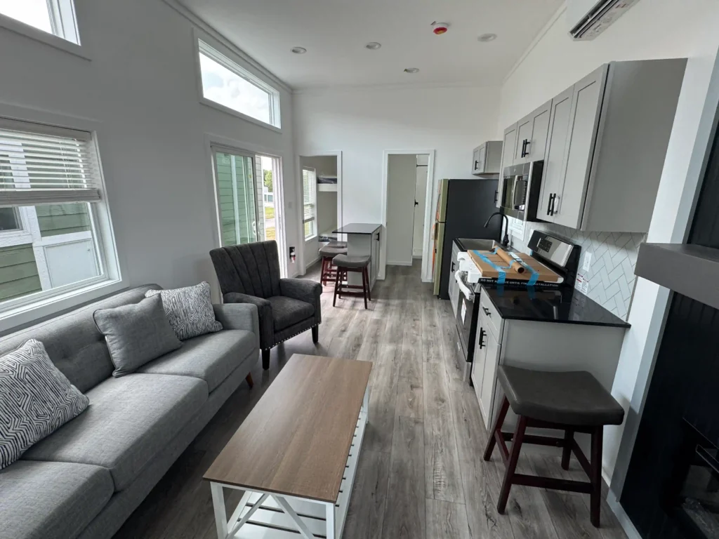 Bright living room layout in a custom park model cottage with grey armchairs, a sofa, and high clerestory windows.