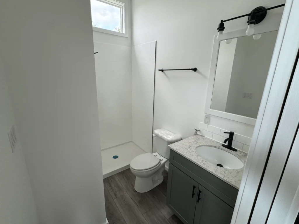 Modern park model bathroom featuring a glass walk-in shower panel, grey vanity, and black fixtures.
