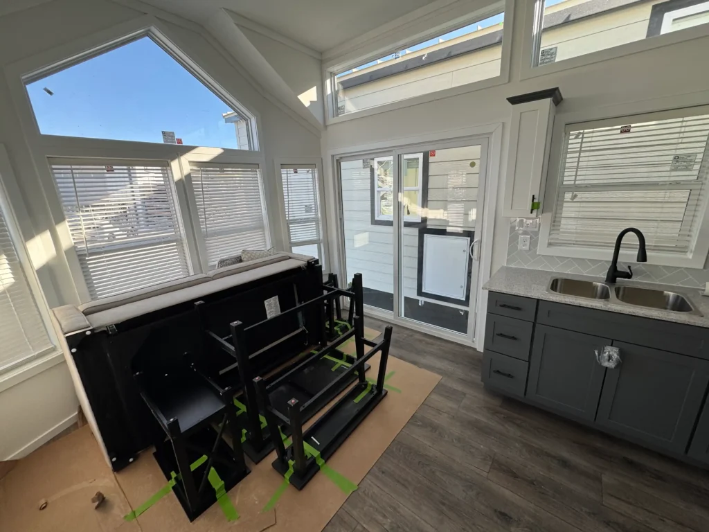 Bright open-concept park model living room with a geometric front window wall, dark flooring, and a kitchen sink.