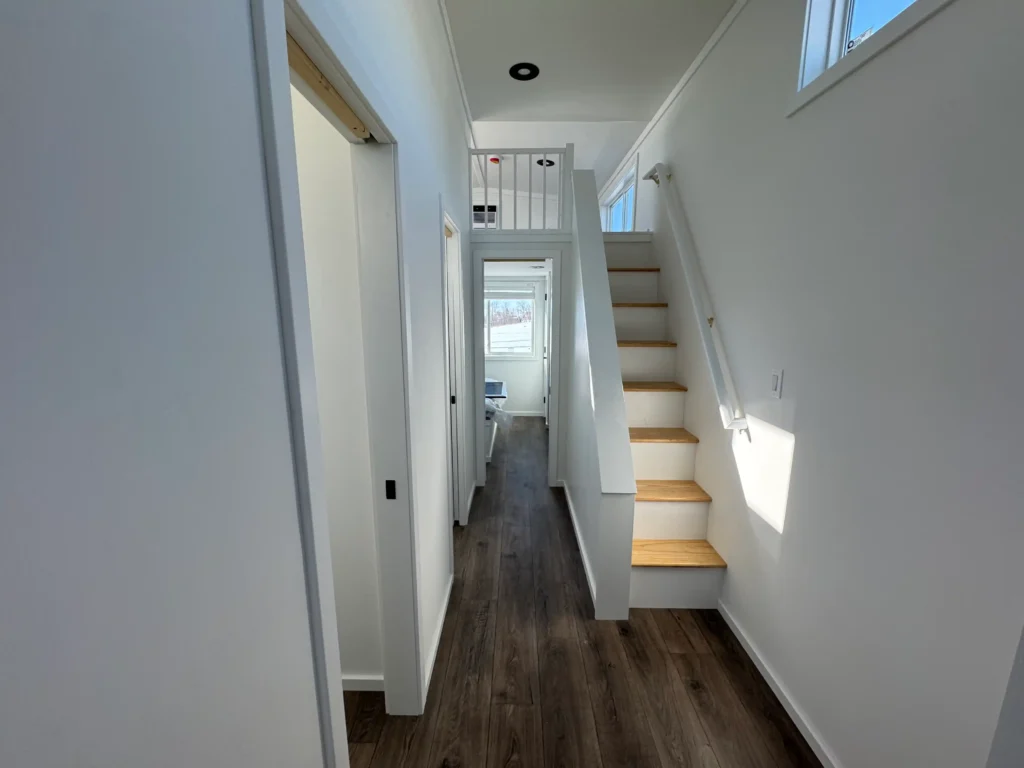 An interior hallway in a custom park model cottage showcasing a permanent wood-tread staircase up to the guest loft.