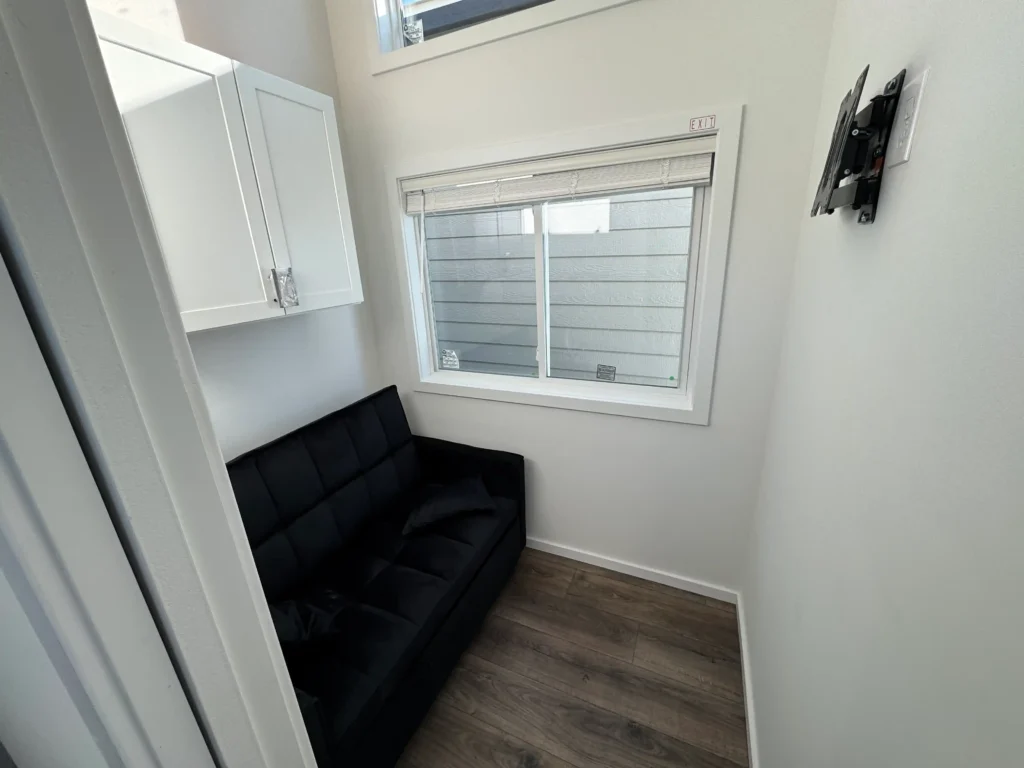 Cozy sitting nook layout in a park model RV featuring a black futon sofa and matching upper white storage cabinets.