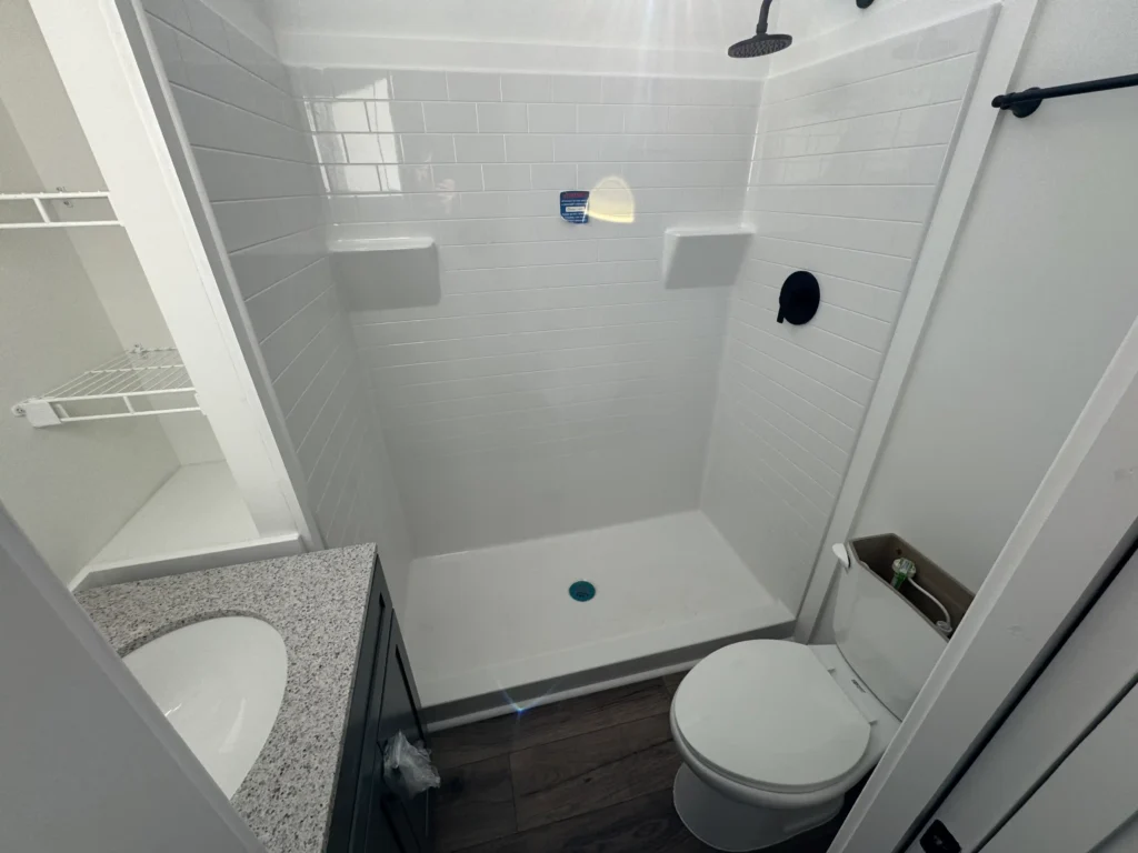 A modern tiny home bathroom layout featuring a white subway tile walk-in shower, granite vanity, and toilet.