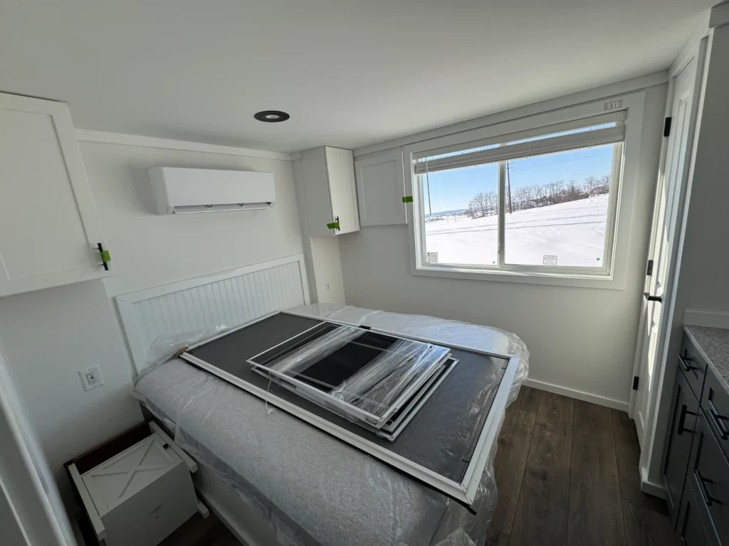 Main bedroom inside a park model cottage showing a queen bed frame, built-in storage cabinets, and a scenic window.