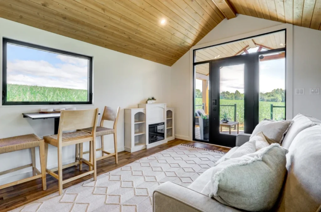 Luxury tiny home interior showcasing cathedral pine ceilings, large windows, and a built-in fireplace.