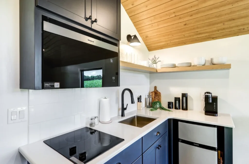 Modern galley kitchen in a Pillar Cabins park model featuring navy blue cabinets and floating shelves.