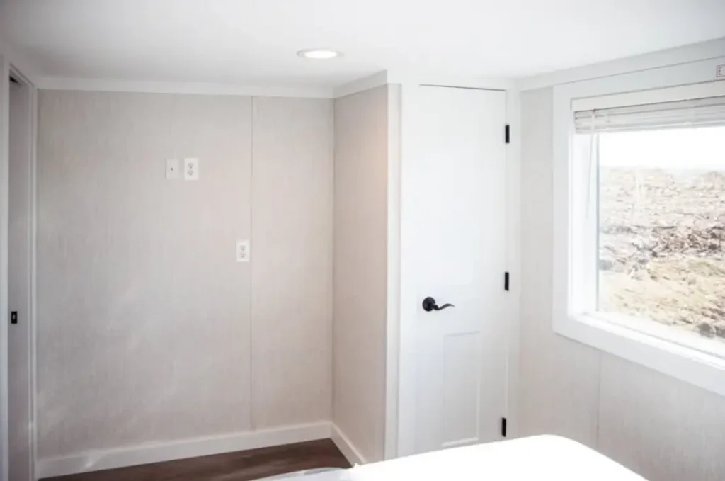 Park model bedroom featuring built-in storage cabinets, a white paneled door, and neutral walls.