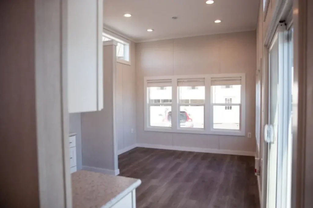 Open concept living room layout with large windows, bright recessed lighting, and a sliding glass entry door.